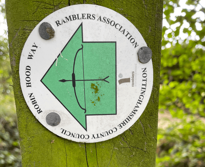 Signpost indicating the Robin Hood Way, featuring a green arrow and bow symbol, affixed to a tree in Nottinghamshire.