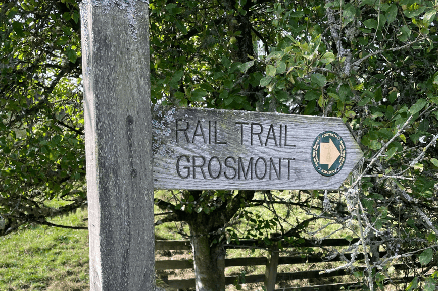Wooden signpost indicating the Rail Trail to Grosmont, surrounded by greenery.