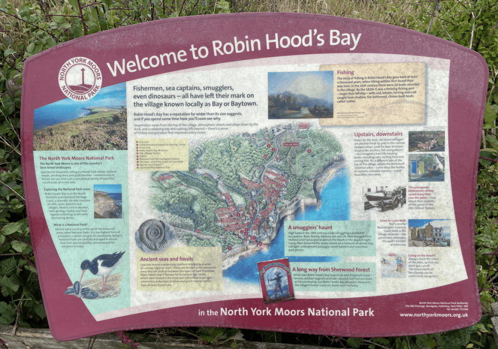 Information sign welcoming visitors to Robin Hood's Bay, highlighting its history, notable figures, and attractions in the North York Moors National Park.