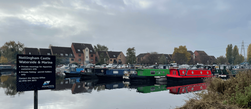 View of Nottingham Castle Waterside and Marina with moored narrowboats on a calm waterway, surrounded by autumn foliage and residential buildings.