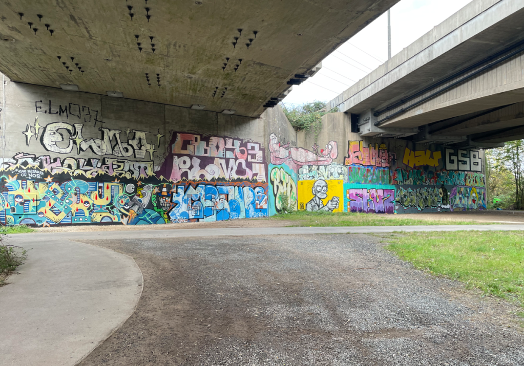 Colourful graffiti covering concrete walls under a bridge, featuring various styles and designs.