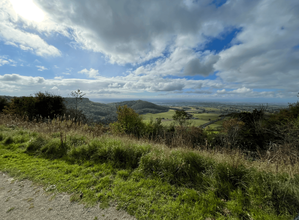 A panoramic view of rolling hills and lush green fields under a partly cloudy sky.