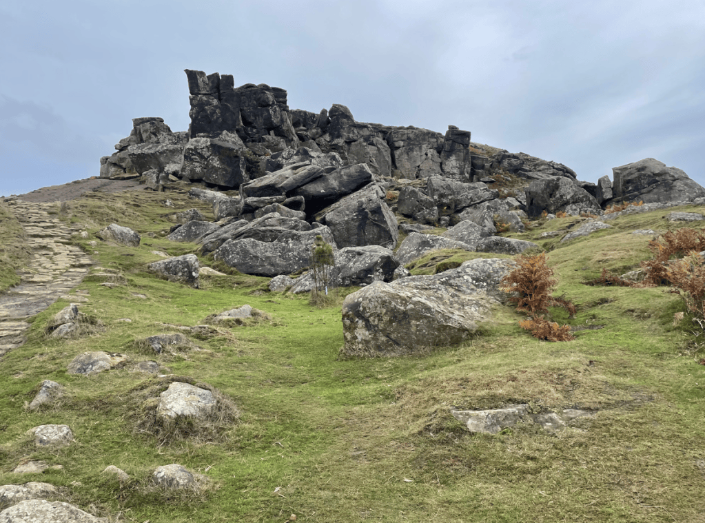 A rocky landscape with large boulders and a pathway leading up a hill, under a cloudy sky.